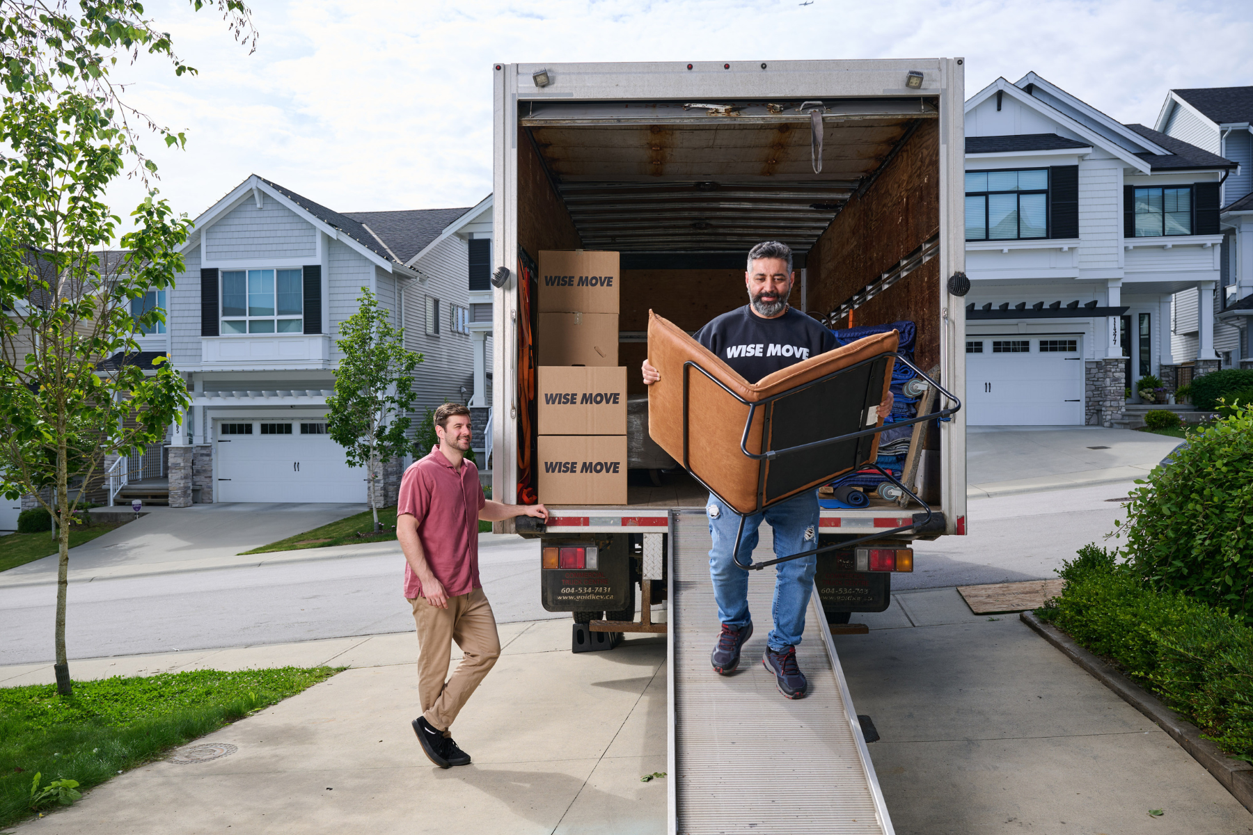 Mover carrying secondhand furniture chair from moving truck while owner watches
