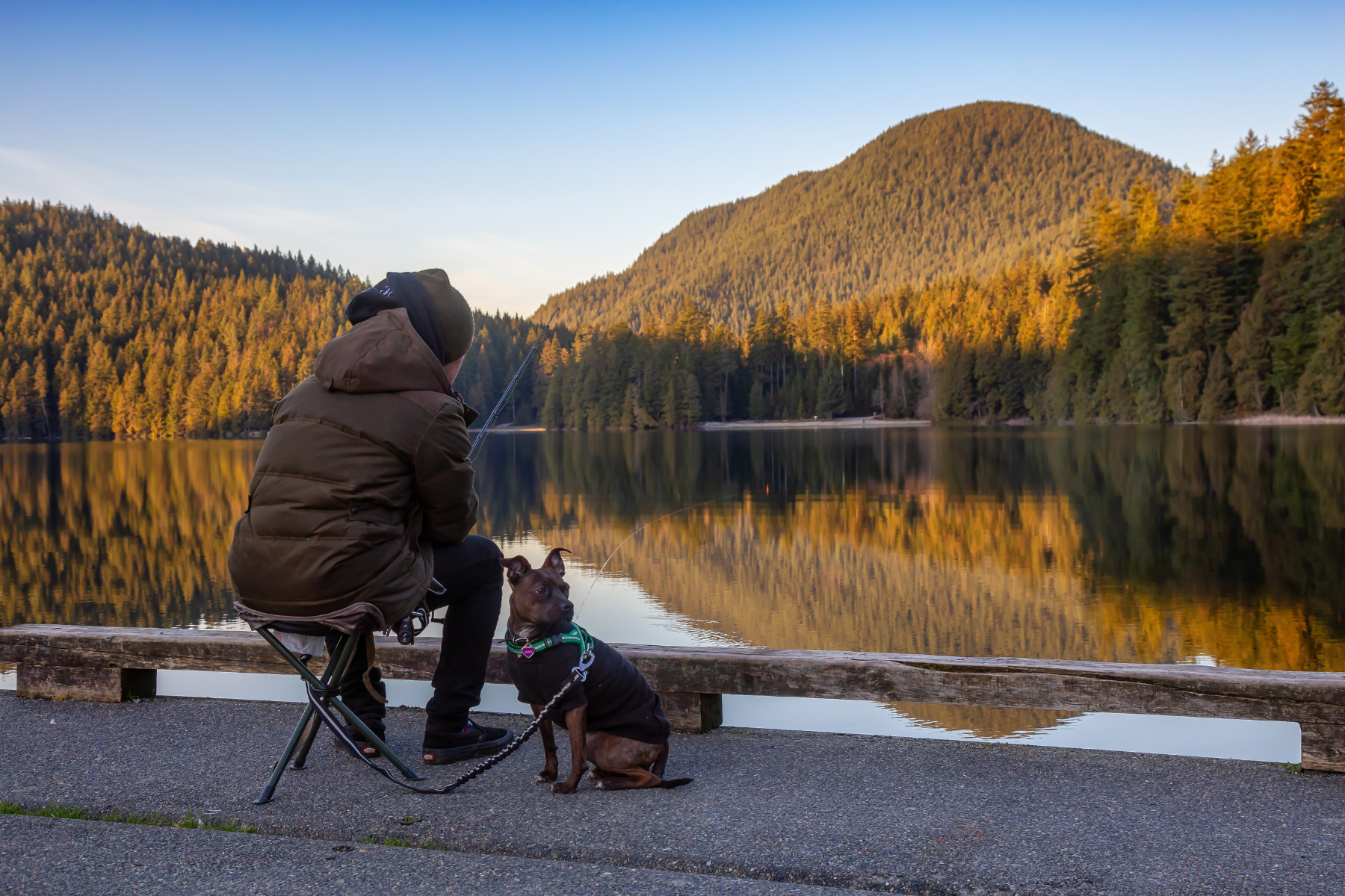 Man with a dog is fishing in the lake at White Pine Beach during a vibrant winter sunset.