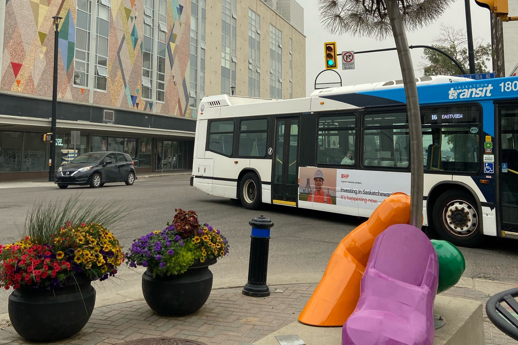A Saskatoon Transit bus passes a colorful public sculpture and mural in downtown Saskatoon