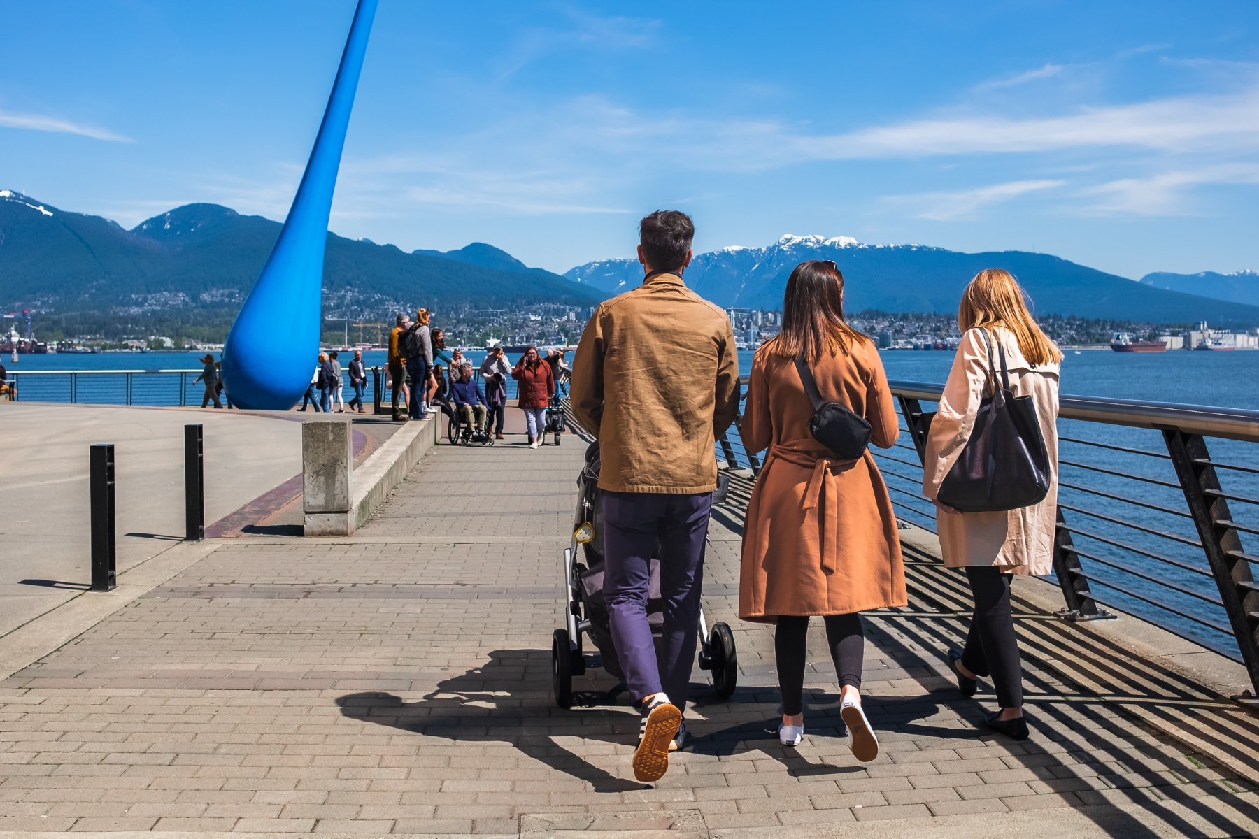 Young family pushing baby stroller and walking on sidewalk at Vancouver urban park Canada