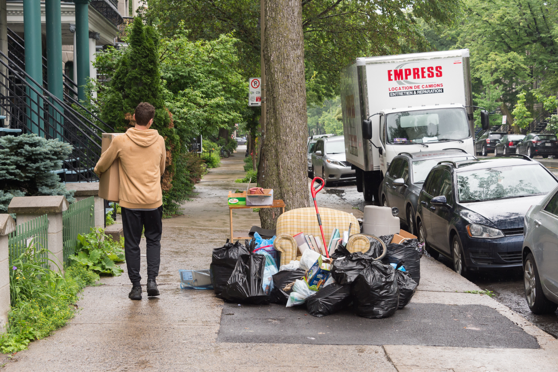 Man carrying a box next to secondhand furniture on curb on Moving Day in Montreal